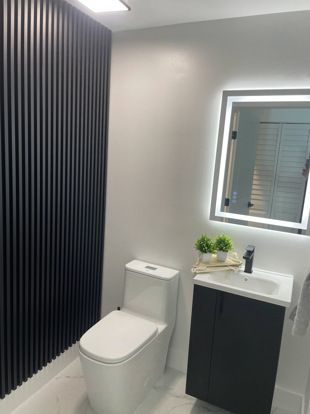 Modern powder room with black slat wall and LED mirror