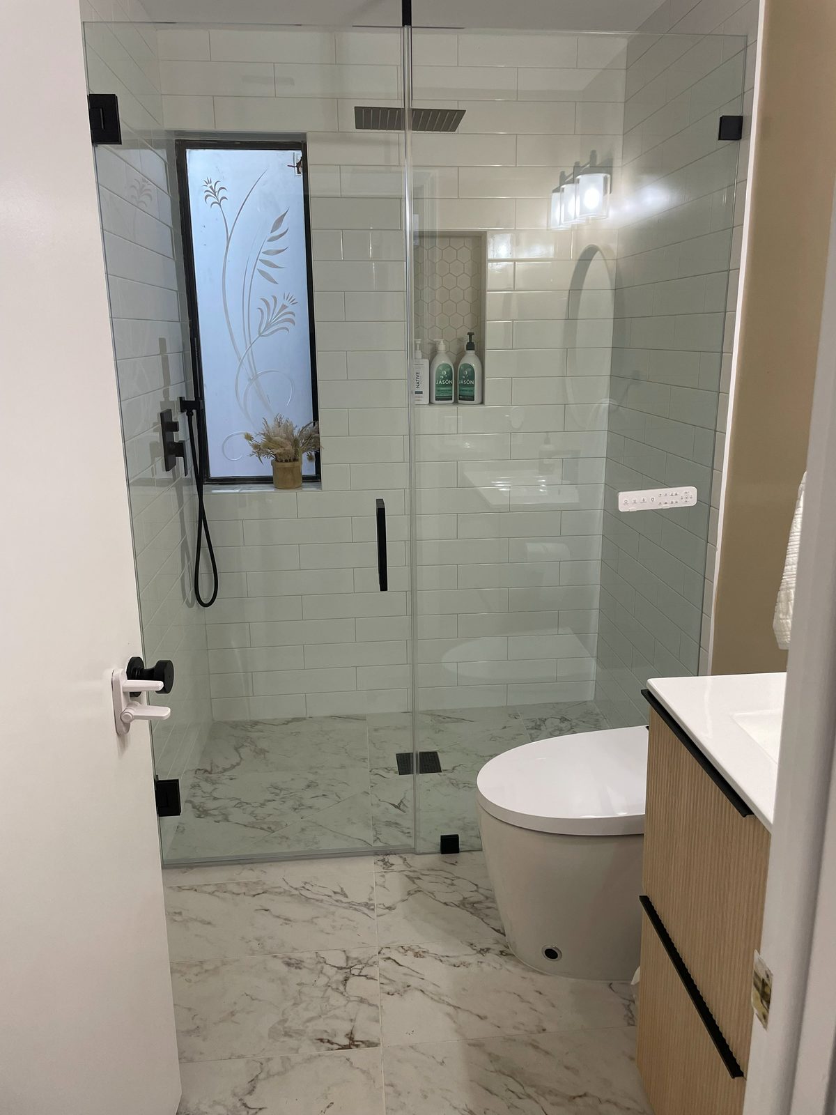 Walk-in glass shower with subway tile and marble floor